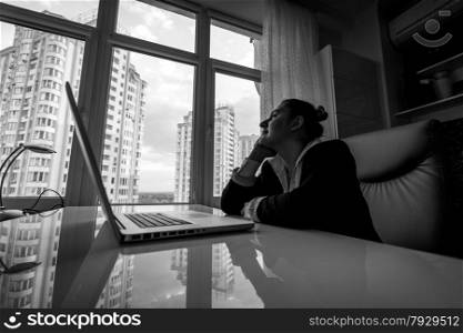 Black and white portrait of dreamy businesswoman looking out of window in office