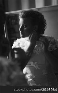 Black and white portrait of elegant bride posing at mirror and wearing earrings
