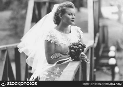 Black and white portrait of elegant bride posing on wooden bridge at windy day