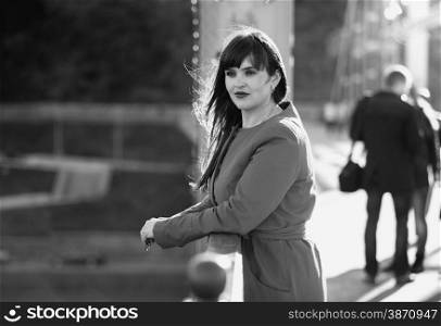 Black and white portrait of elegant woman standing on bridge at windy day