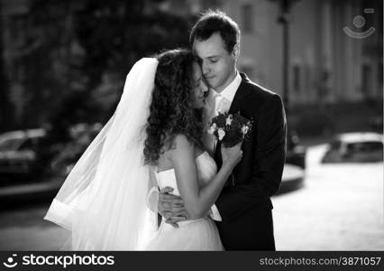 Black and white portrait of embracing bride and groom on street looking at each other