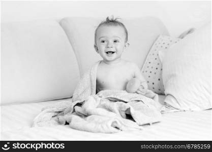 Black and white portrait of funny laughing baby sitting on bed after having bath