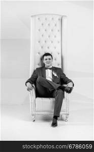 Black and white portrait of handsome stylish man posing at studio in armchair