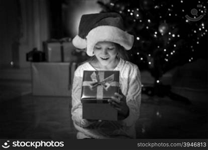Black and white portrait of happy amazed girl looking inside of Christmas present