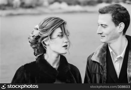 Black and white portrait of happy couple looking at each other with love against the blurred background of a lake. Selective focus.. Monochrome Portrait Of Loving Couple