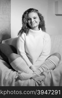 Black and white portrait of happy curly woman in wool sweater and socks sitting on sofa