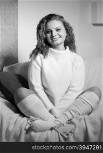Black and white portrait of happy curly woman in wool sweater and socks sitting on sofa