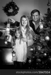 Black and white portrait of happy family posing at Christmas tree with lanterns