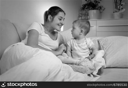 Black and white portrait of happy mother talking with her baby in bed at late evening