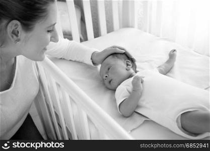 Black and white portrait of happy smiling mother caressing her baby lying in cot