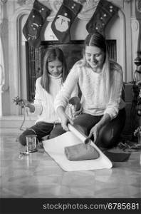 Black and white portrait of happy young mother with daughter wrapping Christmas presents at fireplace