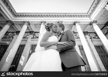 Black and white portrait of just married couple kissing against classic building