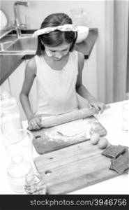 Black and white portrait of little girl rolling raw dough on wooden board