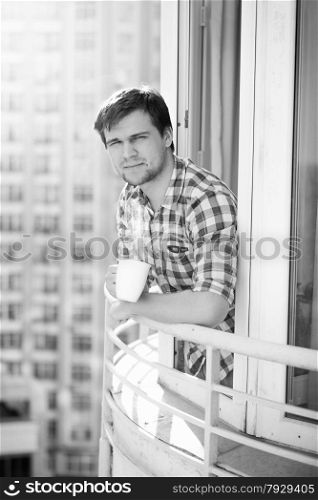 Black and white portrait of man with cup of coffee on balcony
