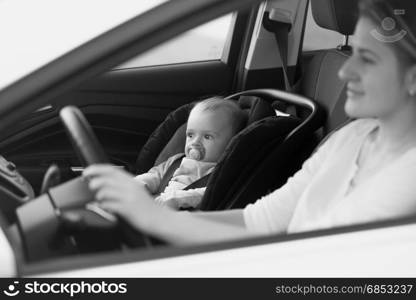 Black and white portrait of mother driving car with her baby sitting on front seat