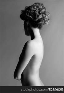 Black and white portrait of sensual nude woman with elegant hairstyle on gray background