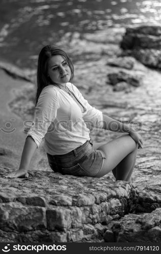 Black and white portrait of sexy woman in white shirt relaxing on big rock on beach