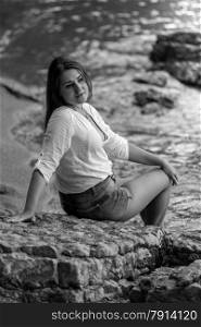 Black and white portrait of sexy woman in white shirt relaxing on big rock on beach