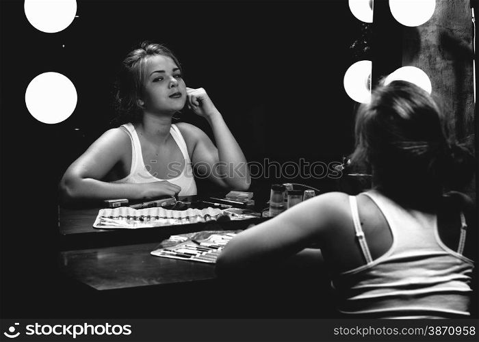 Black and white portrait of sexy woman painting lips at mirror with bulbs