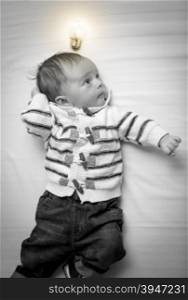 Black and white portrait of smart baby boy with glowing light bulb overhead