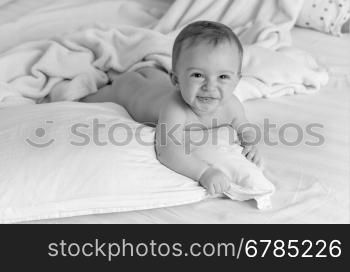 Black and white portrait of smiling naked baby lying on pillows on big bed