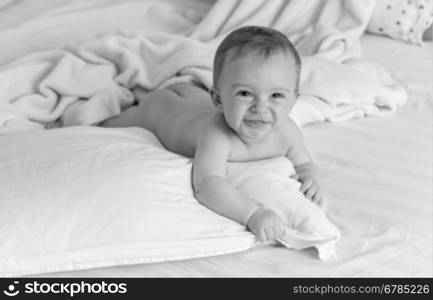 Black and white portrait of smiling naked baby lying on pillows on big bed