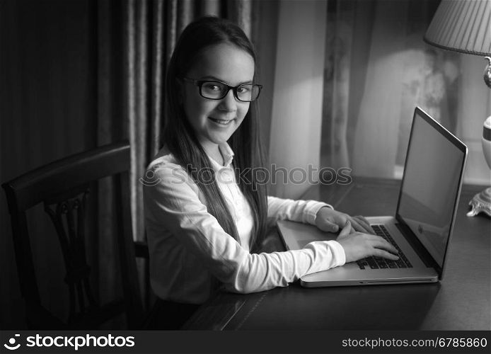 Black and white portrait of smiling schoolgirl using laptop at dark room