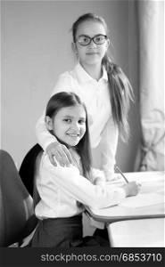 Black and white portrait of two happy schoolgirls doing homework at home