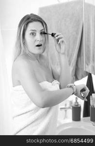 Black and white portrait of woman applying mascara at bathroom and looking at watch