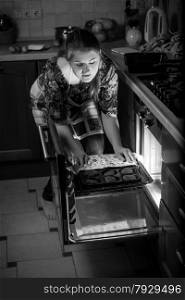 Black and white portrait of woman putting pan in oven