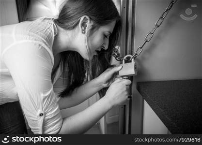 Black and white portrait of woman trying to open lock on fridge