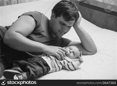 Black and white portrait of young father lying on bed with his newborn baby