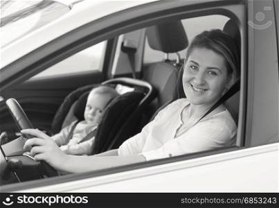 Black and white portrait of young mother driving car with her little baby on front seat
