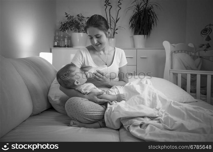 Black and white portrait of young mother feeding her baby at night from bottle