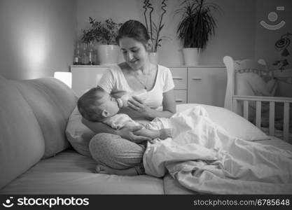 Black and white portrait of young mother feeding her baby at night from bottle