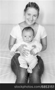 Black and white portrait of young smiling mother sitting with her 3 months old baby