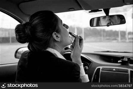 Black and white portrait of young woman applying lipstick in car