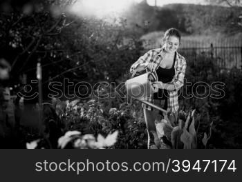 Black and white portrait of young woman working in garden and watering plants