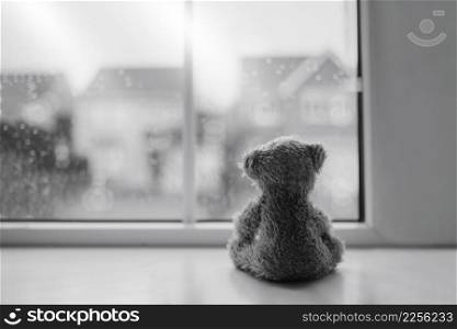 Black and white Rear view Lonely bear doll sitting alone looking out of window, Sad teddy bear sitting next to window in rainy day, lost toy, Loneliness concept, International missing Children day