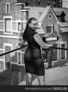 Black and white rear view portrait of elegant slim woman posing against old street