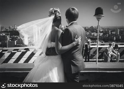 Black and white rear view shot of bride and groom looking at urban city from roof