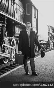 Black and white retro photo of handsome man in suit waiting for train