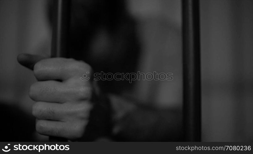 Black and white scene of a heart broken inmate in prison grips bars