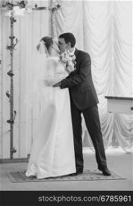 Black and white shot of beautiful bride and groom hugging in hotel hall