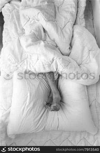 Black and white shot of girls feet lying on pillow at bed