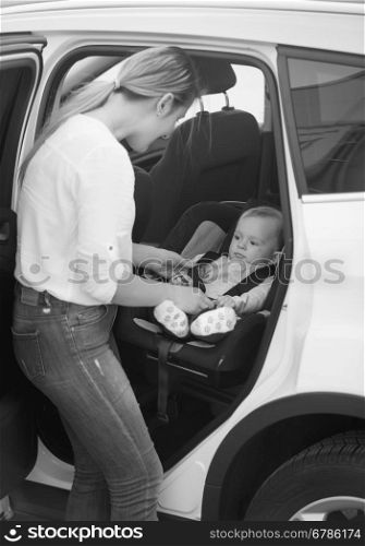 Black and white shot of mother seating her baby boy in car safety seat