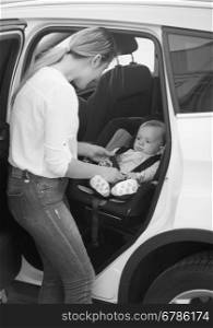 Black and white shot of mother seating her baby boy in car safety seat