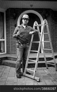 Black and white shot of smiling worker posing with tools at metal ladder