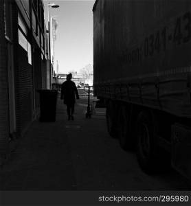black and white silhouette of woman in shadow between wall and truck