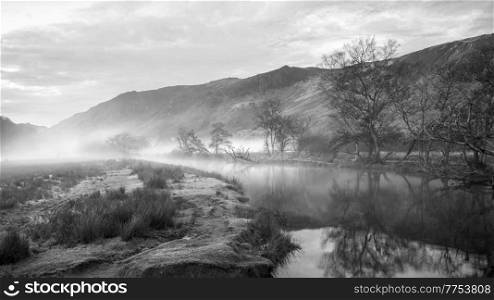 Black and white Stunning Autumn landscape sunrise image looking towards Borrowdale Valley from Derwentwater in Lake District with fog rolling across the landscape